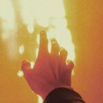 A silhouetted hand reaching towards warm glowing sunlight, creating a dramatic scene.